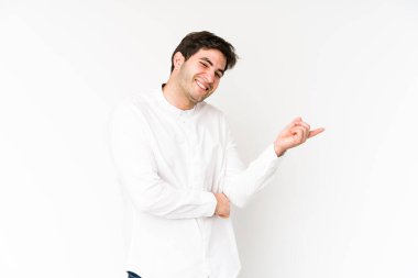 Beyaz arka planda izole edilmiş genç adam işaret parmağıyla işaret ederek gülümsüyor..