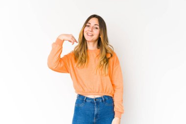 Beyaz arka planda yaşayan beyaz tenli genç bir kadın gömlek fotokopi alanını elle işaret ediyor, gururlu ve kendinden emin