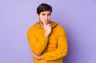 Mor arka planda izole edilmiş genç adam şüpheli ve şüpheci bir ifadeyle yana bakıyor..