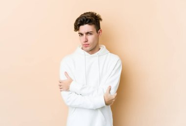 Beyazlı genç adam bej arka planda izole edilmiş. Mutsuz, iğneleyici bir ifadeyle kameraya bakıyor..