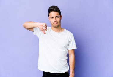 Mor arka planda izole edilmiş genç beyaz bir adam hoş olmayan bir jest yapıyor, başparmakları aşağıda. Anlaşmazlık konsepti.