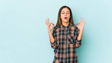 Mavi arka planda izole edilmiş genç bir kadın yoğun bir günün ardından rahatlıyor, yoga yapıyor..