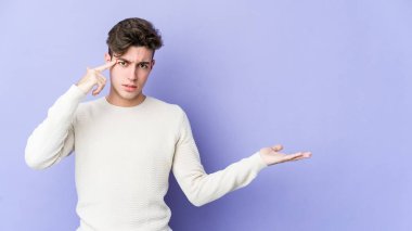 Mor arka planda izole edilmiş genç beyaz adam elinde bir ürün tutuyor..