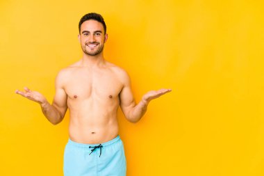 Sarı arka planda mayosu olan genç beyaz bir adam kolları olan beyaz tenli genç bir adam, mutlu ve kendinden emin hissediyor..
