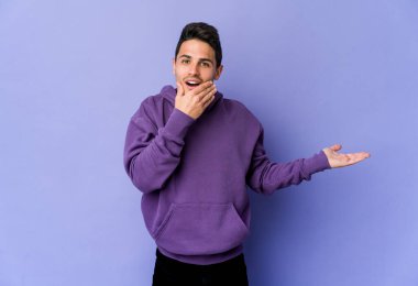 Mor arka planda izole edilmiş genç beyaz bir adam avuç içinde fotokopi alanı tutuyor, el üstünde tutuyor. Şaşırmış ve mutlu..