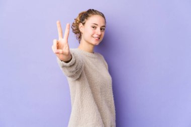 Mor arka planda genç beyaz kadın neşeli ve kaygısız parmakları olan bir barış sembolü gösteriyor..