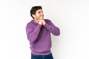 Beyaz arka planda izole genç adam ellerini çenesinin altında tutuyor, mutlu bir şekilde yan tarafa bakıyor..