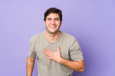 Mor arka planda izole olmuş genç adam kahkahalar atıyor elini göğsüne koyuyor..