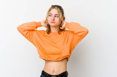 Beyaz arka planda genç beyaz kadın kendini güvende hissediyor, elleri başının arkasında..