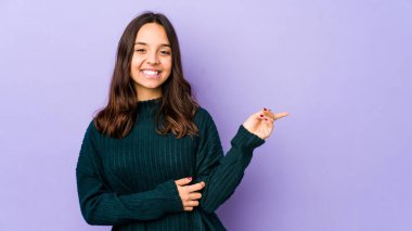 Latin kökenli genç bir kadın izole edilmiş, neşeli bir şekilde işaret parmağıyla işaret ederek gülümsüyor..