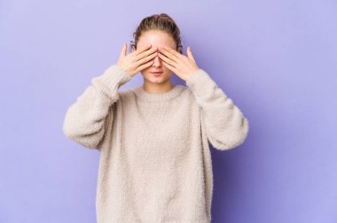 Mor arka planda genç beyaz bir kadın elleriyle gözlerini kapatmaktan korkuyor..
