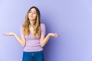 Mor arka planda soyutlanmış beyaz bir kadın sorgulama sırasında omuz silkiyor ve şüphe duyuyor..