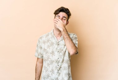 Beyaz tenli genç adam bej arka planda izole edilmiş gülerek, kaygısız, doğal duygularla gülüyor..