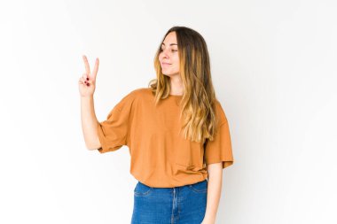 Beyaz arka planda izole edilmiş genç beyaz kadın neşeli ve kaygısız parmakları olan bir barış sembolü gösteriyor..