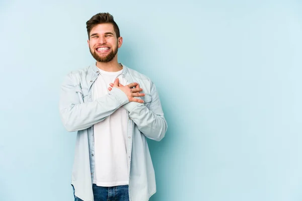 青い背景に孤立した若い白人男性が手を心に留めて笑い 幸福の概念 — ストック写真