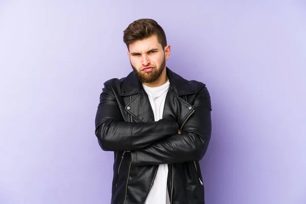 Young man isolated on purple background frowning face in displeasure, keeps arms folded.