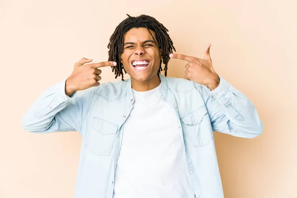 Young african american rasta man smiles, pointing fingers at mouth.