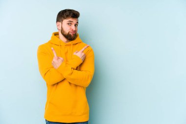 Mavi arka plan noktalarında izole genç beyaz adam, iki seçenek arasında seçim yapmaya çalışıyor.