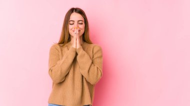 Pembe arka planda soyutlanmış genç beyaz bir kadın el ele tutuşup ağzının kenarında dua ediyor, kendinden emin hissediyor..