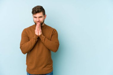 Kafkasyalı genç bir adam mavi arka planda izole edildi. Aklında bir plan kuruyor, bir fikir kuruyor..
