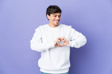 Genç havalı adam gülümsüyor ve elleriyle kalp şeklini gösteriyor..