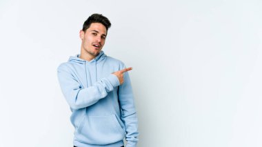 Beyaz arka planda izole edilmiş genç beyaz bir adam gülümsüyor ve boş alanda bir şeyler gösteriyor..