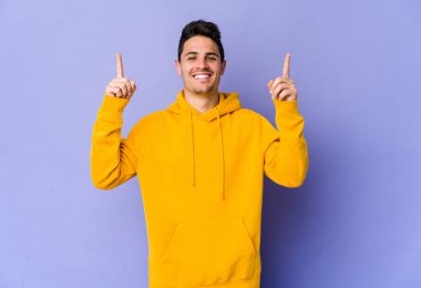 Mor arka planda izole genç beyaz adam iki ön parmağı da boş bir alan gösteriyor..