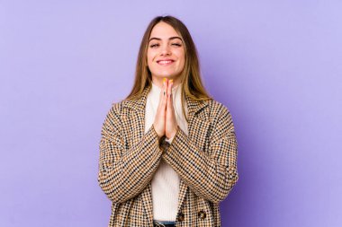 Mor arka planda izole edilmiş genç beyaz bir kadın el ele tutuşup, ağız kenarında dua ediyor, kendinden emin hissediyor..