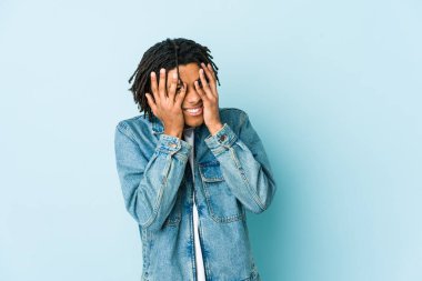 Kot ceket giyen genç siyahi adam kameraya parmaklarıyla göz kırpıyor, yüzünü kapatmaktan utanıyor..