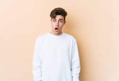 Beyazlı genç bir adam bej arka planda izole edilmiş. Gördüğü bir şey yüzünden şok oluyor..