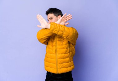 Mor arka planda izole genç beyaz adam iki kolu çapraz tutuyor, inkar kavramı.