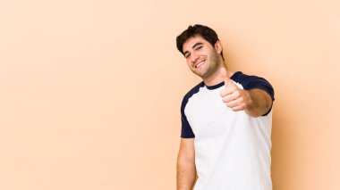 Bej arka planda izole edilmiş genç adam gülümsüyor ve baş parmağını kaldırıyor.