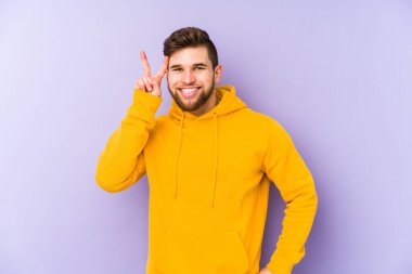 Mor arka planda izole edilmiş genç bir adam iki numarayı parmaklarıyla gösteriyor..