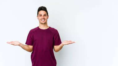 Beyaz arka planda izole genç beyaz adam kollarıyla ölçek yapar, mutlu ve kendinden emin hisseder..