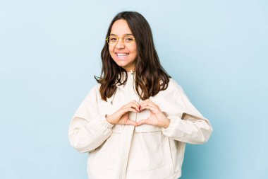 Latin kökenli genç bir kadın izole edilmiş gülümsüyor ve elleriyle kalp şeklinde bir şey gösteriyor..