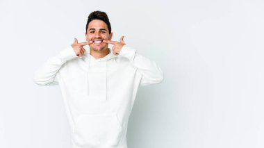 Beyaz arka planda izole edilmiş genç beyaz adam gülümsüyor, parmaklarını ağıza doğrultuyor..