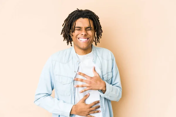 Young african american rasta man laughs happily and has fun keeping hands on stomach.