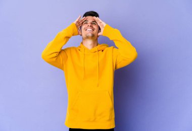 Mor arka planda izole edilmiş genç beyaz adam, mutlu bir şekilde ellerini başının üstünde tutarak gülüyor. Mutluluk kavramı.