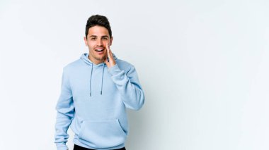 Beyaz arka planda izole genç beyaz adam yüksek sesle bağırıyor, gözleri açık ve elleri gergin tutuyor..