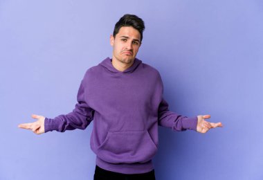 Mor arka planda izole edilmiş genç beyaz adam sorgulama sırasında omuz silkiyor ve şüphe duyuyor..