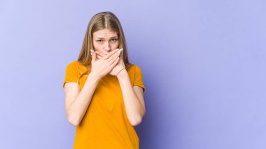 Mor arka planda izole edilmiş genç sarışın kadın elleri endişeli bir şekilde ağzı örtüyor..
