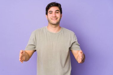 Mor arka planda izole genç bir adam iki eliyle bir şey tutuyor, ürün sunumu..