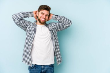 Kafkasyalı genç adam mavi arka planda izole edilmiş. Kendine güveniyor, elleri başının arkasında..