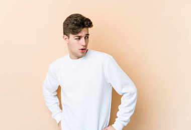 Beyaz tenli, bej arka planda izole bir genç. Gülümsüyor, neşeli ve keyifli görünüyor..