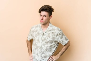 Beyazlı genç bir adam bej arka planda izole edilmiş hoşnutsuzca kaşlarını çatmış, kollarını kavuşturmuş..