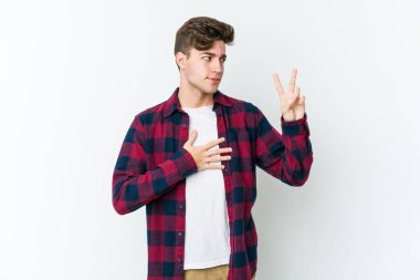 Beyaz arka planda izole edilmiş genç beyaz adam yemin ediyor, elini göğsüne koyuyor..