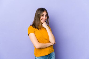 Genç beyaz kadın mutlu ve kendinden emin gülümsüyor, elleriyle çenesine dokunuyor..