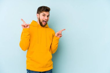 Mavi arka planda izole edilmiş genç beyaz adam farklı kopya alanlarını gösteriyor, birini seçiyor, parmaklarıyla gösteriyor.