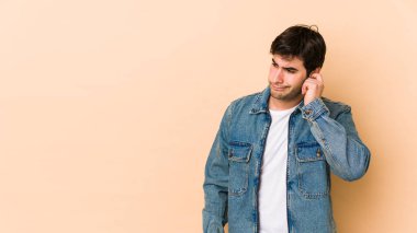 Genç adam bej arka planda izole edilmiş parmaklarıyla kulaklarını kapatan, yüksek sesli bir ortam tarafından stresli ve çaresiz.