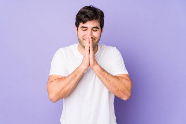 Mor arka planda izole olmuş genç bir adam. El ele tutuşup, ağzının kenarında dua ediyor. Kendine güveniyor..